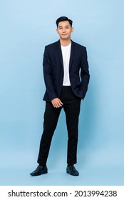 Full Length Portrait Of Smiling Young Handsome Asian Man In Semi Formal Suit Standing With One Hand In Pocket On Light Blue Studio Background