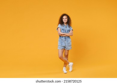 Full length portrait of smiling young african american girl in denim clothes isolated on yellow wall background studio portrait. People lifestyle concept. Mock up copy space. Holding hands crossed - Powered by Shutterstock