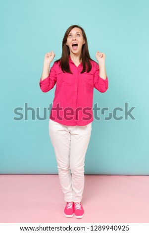 Full length portrait of smiling young pretty woman in rose shirt blouse, white pants posing isolated on bright pink blue pastel wall background studio. Fashion lifestyle concept. Mock up copy space