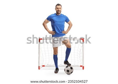 Full length portrait of a soccer player posing with a ball in front of a mini goal isolated on white background