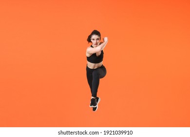 Full Length Portrait Of Strong Powerful Young Fitness Sporty Woman Wearing Black Sportswear Posing Training Working Out Jumping Like Running Looking Camera Isolated On Orange Color Background Studio