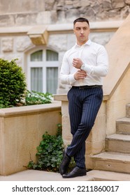 Full Length Portrait Of Stylish Man Groom Posing Along Dressed In White Shirts And Dark Blue Pants. Handsome Groom Man Standing On Stairs Outdoors Looking Ahead. Wedding. Waiting For Bride.