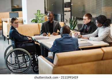 Full length portrait of successful businesswoman using wheelchair at meeting and talking to colleagues in modern office space - Powered by Shutterstock