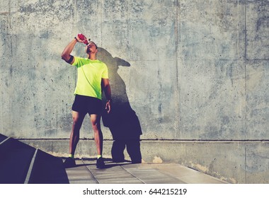 Full length portrait of sweaty man runner refreshing with energy drink water after jogging against cement wall background with copy space area for your text message or content,sportsman having a rest 