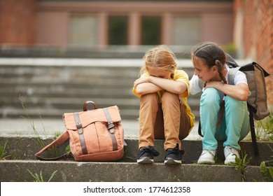 Full length portrait of teenage schoolgirl crying while sitting on stairs outdoors with smiling friend comforting her, copy space - Powered by Shutterstock