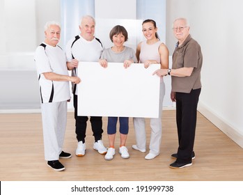 Full length portrait of trainer and senior customers holding blank billboard at healthclub - Powered by Shutterstock