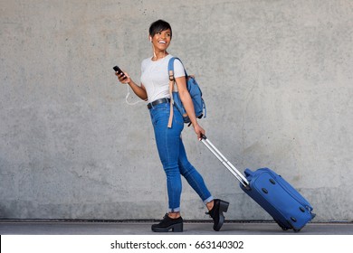 Full length portrait of traveling young woman with mobile phone and suitcase