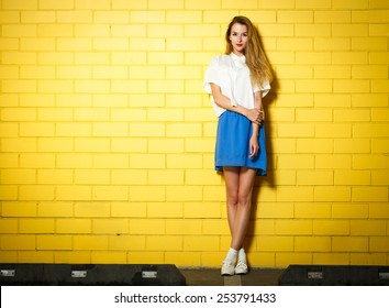 Full Length Portrait of Trendy Hipster Girl Standing at the Yellow Brick Wall Background. Urban Fashion Concept. Copy Space.