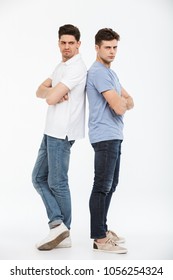 Full Length Portrait Of Two Angry Young Men Standing Back To Back With Arms Folded Isolated Over White Background