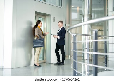 Full length portrait of two business people, man and woman, chatting cheerfully while waiting for elevator in office building, copy space - Shutterstock ID 1090634261