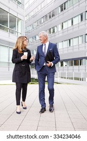 Full Length Portrait Of Two Business People Walking And Talking Next To An Office Building After A Successful Business Meeting. 