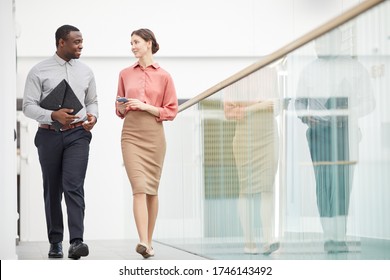 Full length portrait of two contemporary business people walking towards camera and talking in minimal office building interior, copy space