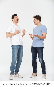 Full Length Portrait Of Two Handsome Young Men Talking And Laughing Isolated Over White Background