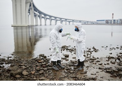 Full Length Portrait Of Two People Wearing Hazmat Suit Standing By Water, Toxic Waste And Pollution Concept, Copy Space