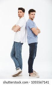 Full Length Portrait Of Two Upset Young Men Standing Back To Back With Arms Folded Isolated Over White Background