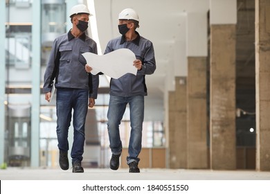 Full Length Portrait Of Two Workers Wearing Masks And Holding Plans While Walking Towards Camera At Construction Site, Copy Space