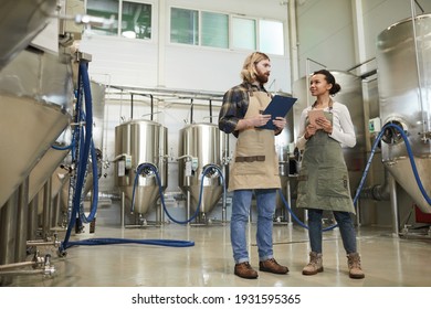 Full length portrait of two young workers wearing aprons looking at each other while standing at brewery workshop, copy space - Powered by Shutterstock