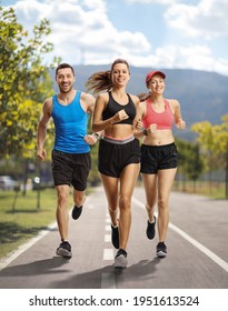 Full length portrait of two young females and a guy in sportswear running on an asphalt lane 