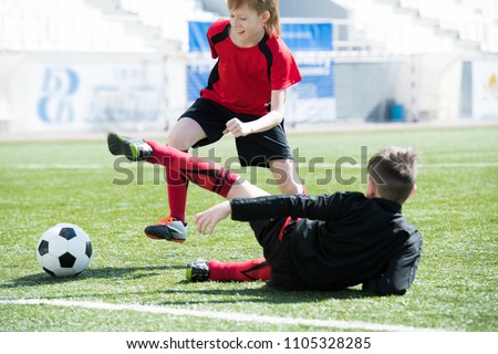 Full length portrait of unrecognizable teenage boy falling on grass after being attacked by another player on football field during junior team practice