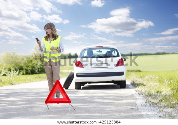 Full length portrait of woman\
standing her breaking down car and calling roadside assistance.\
