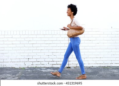 Full length portrait of woman walking on sidewalk with headphones and purse - Shutterstock ID 451319695