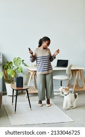 Full Length Portrait Of Young African American Woman Dancing To Music At Home Using Smart Speaker With AI Technology