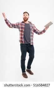 Full length portrait of a young bearded man actor in plaid shirt holding book and gesturing with hands over white background