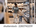 Full length portrait of young black mother in supermarket shopping for groceries with little girl and pushing cart