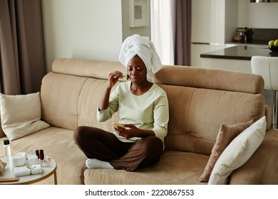 Full length portrait of young black woman watching face massage tutorial while enjoying self care day at home