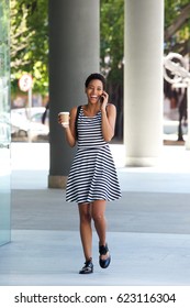 Full Length Portrait Of Young Black Woman Walking In City With Mobile Phone 