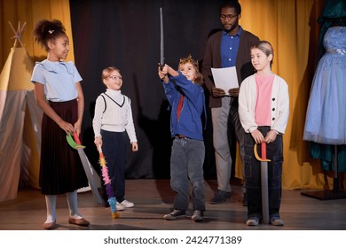 Full length portrait of young boy playing valiant prince on stage in school play with group of children - Powered by Shutterstock