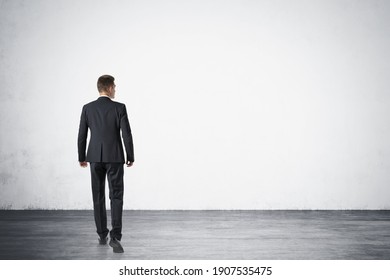 Full Length Portrait Of Young Businessman Walking Forward In Empty Concrete Wall Room. Rear View. Mock Up