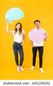 Full length portrait of young couple man and woman standing together while holding blank thought bubbles isolated over yellow background