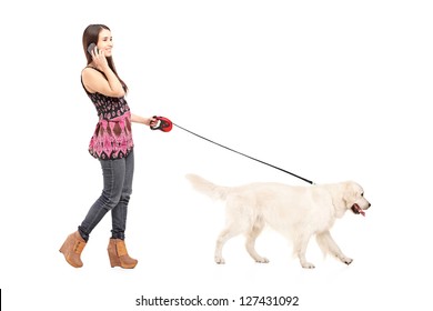 Full Length Portrait Of A Young Female Walking Her Dog And Talking On A Mobile Phone Isolated On White Background