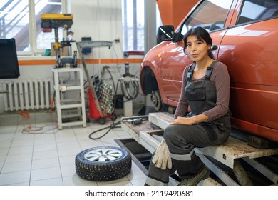 Full length portrait of young female mechanic looking at camera while changing tires in car repair workshop, copy space - Powered by Shutterstock