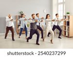 Full length portrait of young funny business people doing corporate exercises standing at workplace in office. Team of smiling company employees exercising for health during a break from a work.