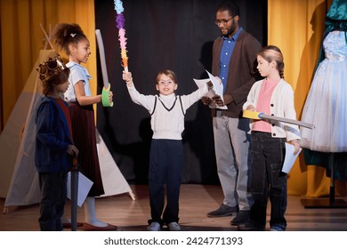 Full length portrait of young girl standing on stage rehearsing school play with group of children in theater - Powered by Shutterstock