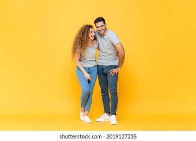 Full Length Portrait Of Young Happy Interracial Millennial Couple Holding Each Other And Laughing In Isolated Yellow Studio Background