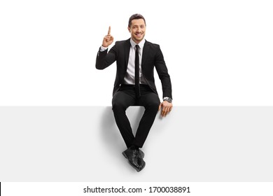 Full length portrait of a young man in a suit sitting on a panel and pointing upwards isolated on white background - Powered by Shutterstock