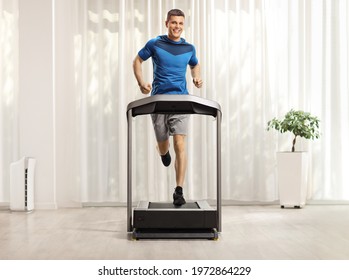 Full Length Portrait Of A Young Man Running On A Treadmill At Home