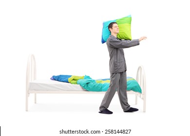 Full Length Portrait Of A Young Man In Pajamas Sleepwalking By His Bed Isolated On White Background