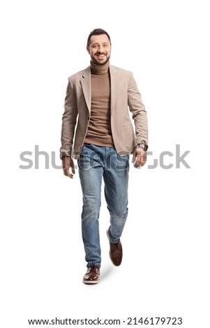 Full length portrait of a young man in a beige suit and jeans walking towards camera isolated on white background