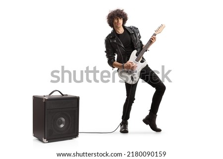 Full length portrait of a young rock musician playing a guitar plugged into an amplifier isolated on white background