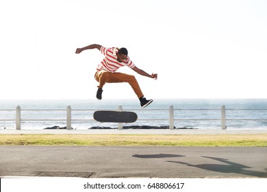 Full length portrait of a young skateboarder doing tricks and jumping on the road by the beach - Powered by Shutterstock