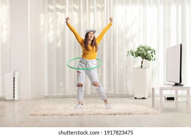 Full Length Portrait Of A Young Woman Spinning A Hula Hoop At Home In A Living Room