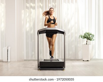 Full length portrait of a young woman in shorts and top running on a treadmill at home - Powered by Shutterstock