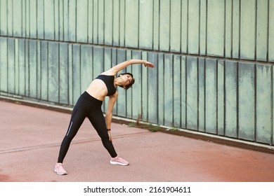 Full Length Portrait Of Young Woman Doing Stretching Exercise Outside In The City