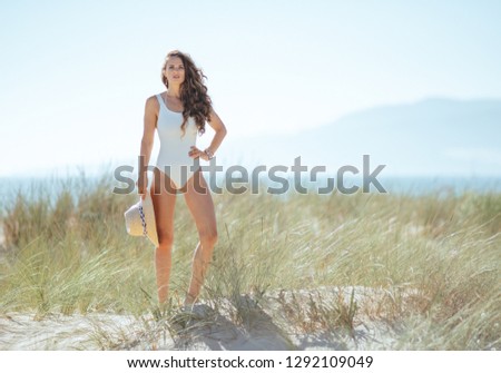 Full length portrait of young woman in white swimwear on the beach.woman holding straw hat. stressed free beach retreat. quiet vacation heaven. minimal to no crowd peace. european woman. blue sky.