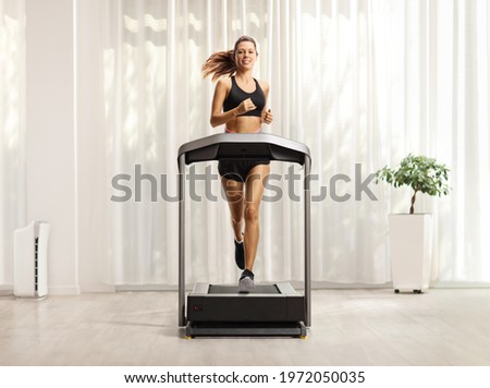 Full length portrait of a young woman in shorts and top running on a treadmill at home