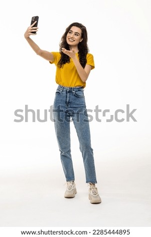 Full length portrait of a young woman taking a selfie and showing peace gesture isolated over white background